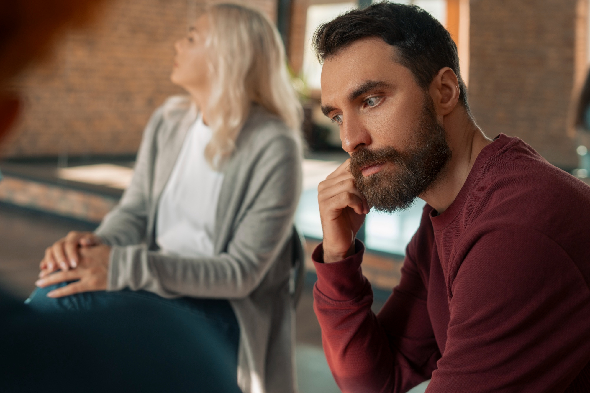 A man looking unhappy while a woman sits next to him and someone else appears in front | Source: Freepik