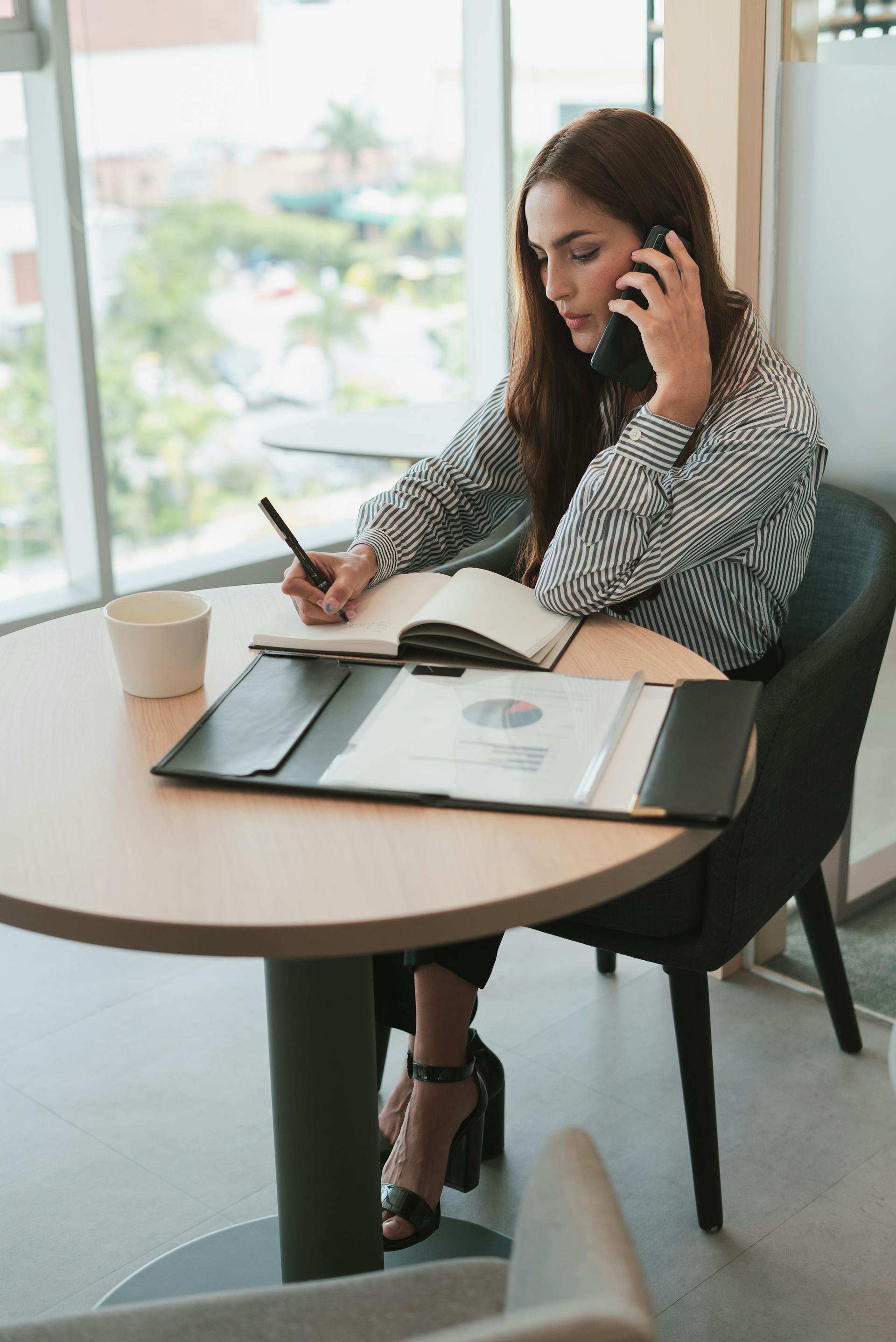 A woman talking on the phone and writing something in her notebook | Source: Pexels