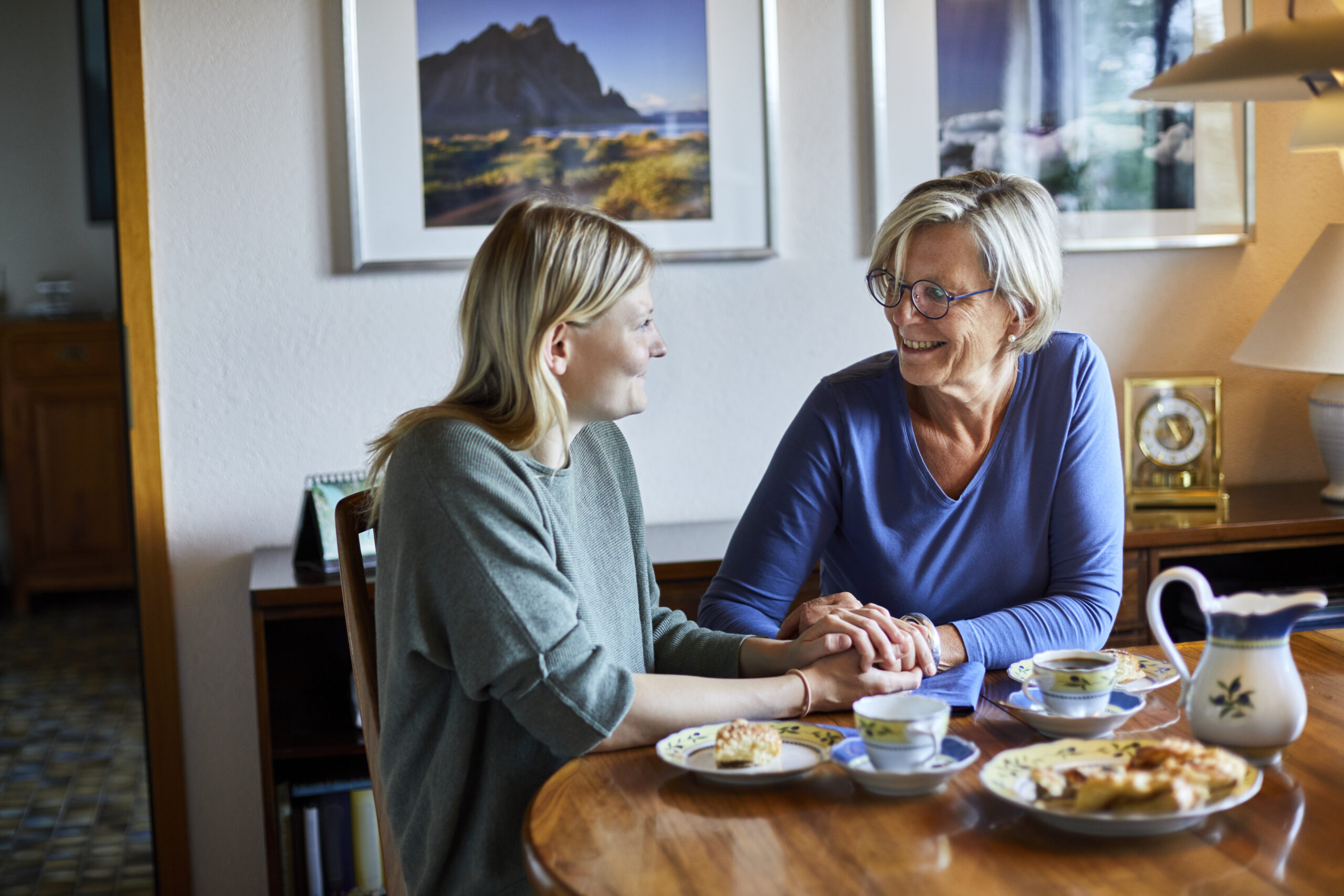 Senior woman and young woman sitting at dining table holding hands | Source: Getty Images