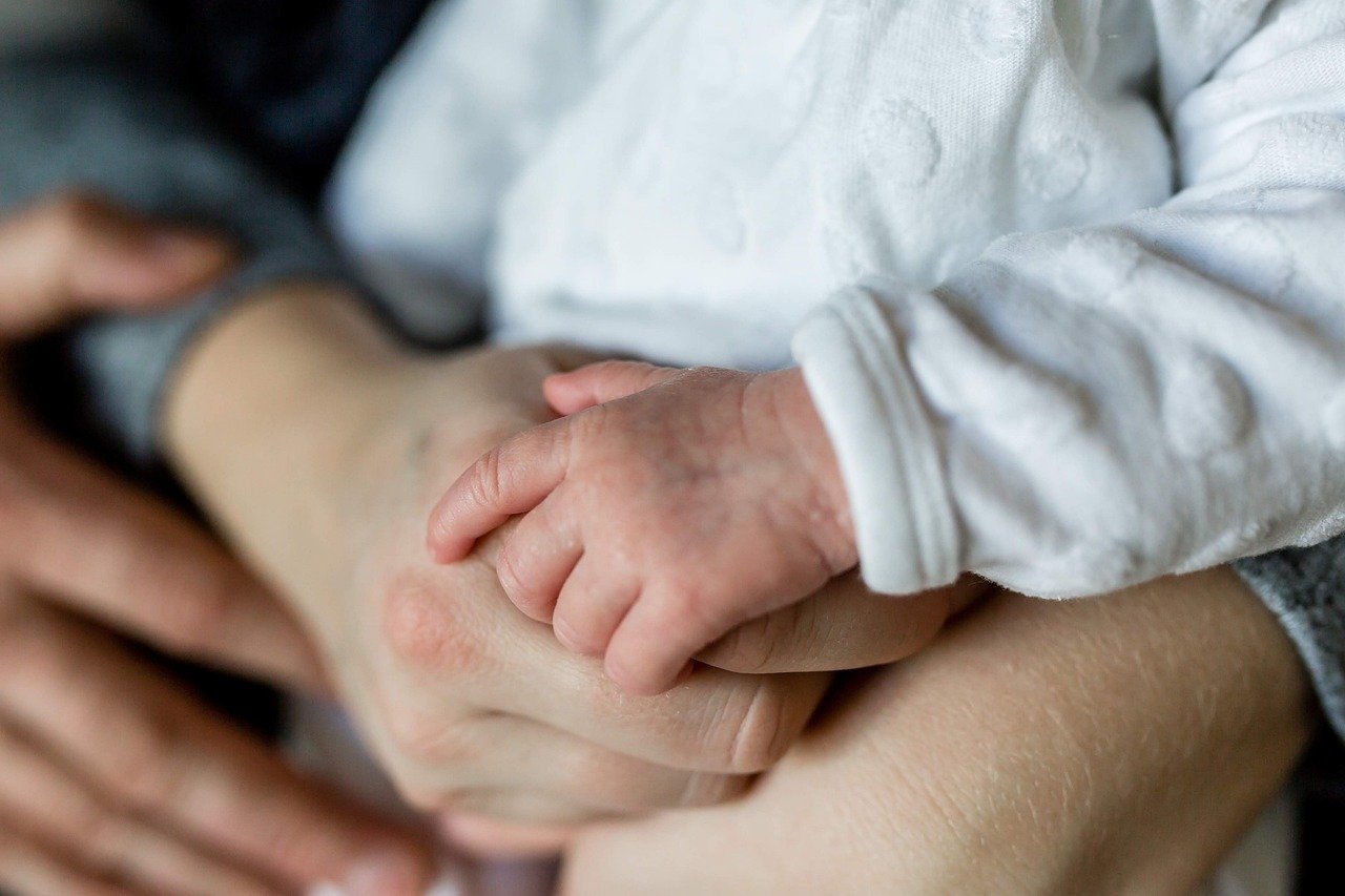 A baby held in the arms of two adults | Source: Pixabay