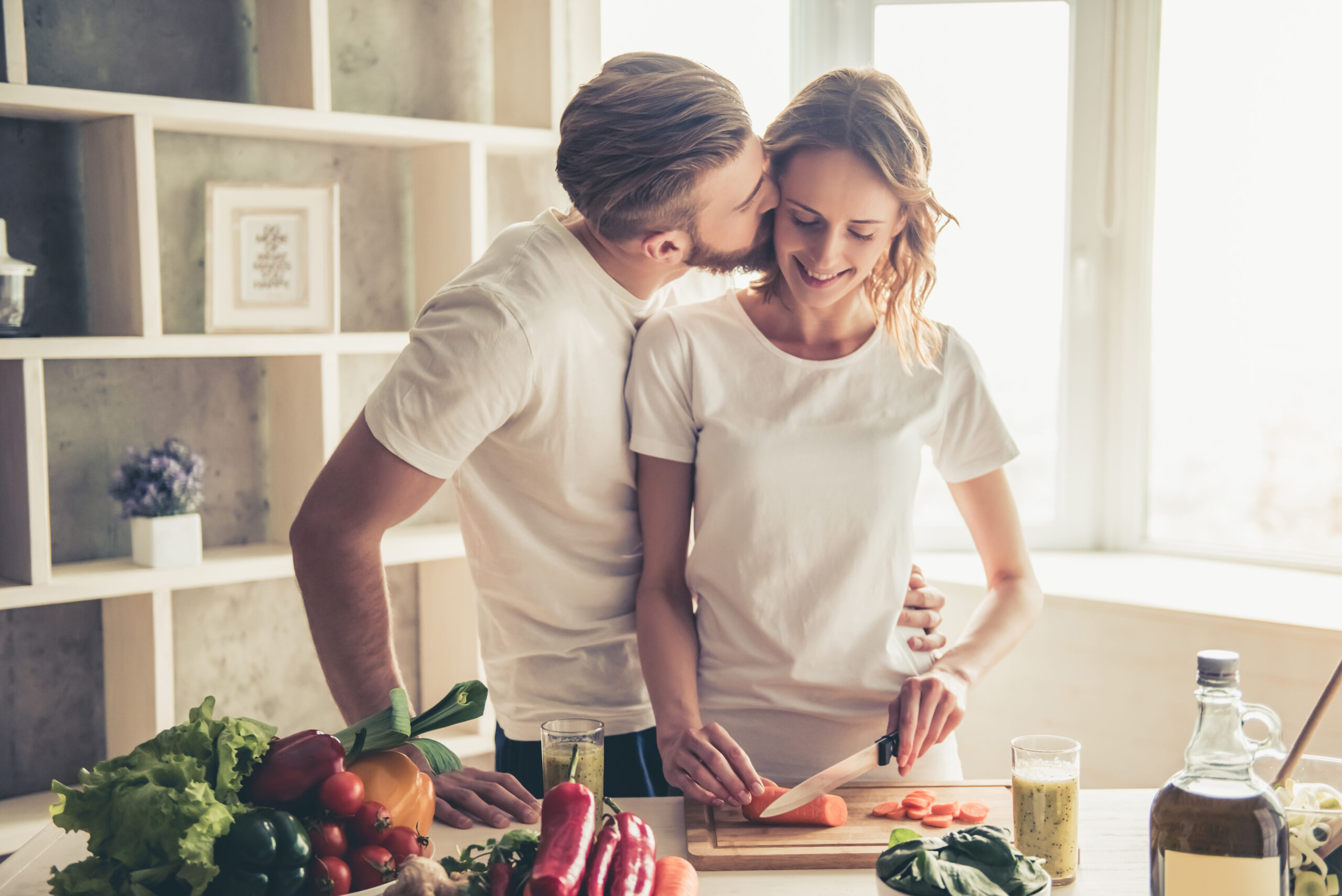 A man kissing his wife while she chops vegetables | Source: Shutterstock