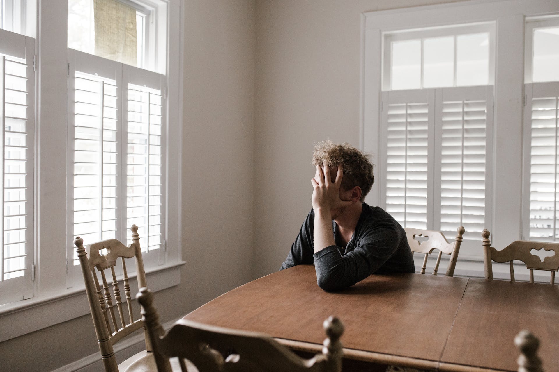 A man sits at a table with his head resting in one hand | Source: Pexels